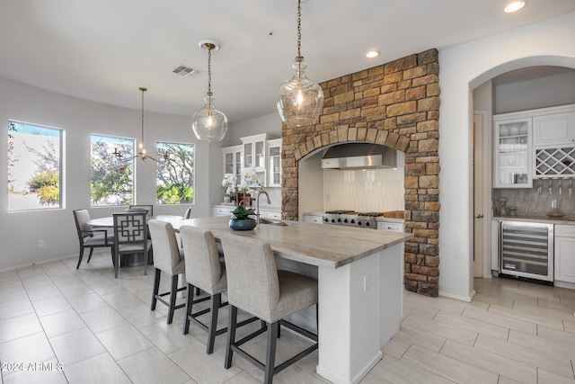 kitchen featuring a kitchen island with sink, wine cooler, white cabinets, and pendant lighting