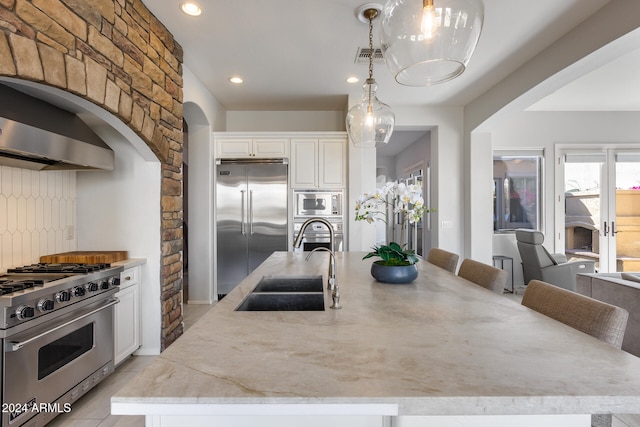 kitchen featuring white cabinetry, premium appliances, decorative light fixtures, and a kitchen island with sink