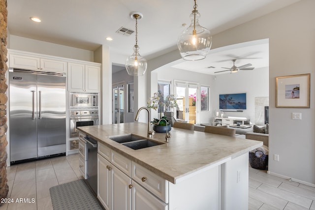 kitchen with sink, white cabinetry, decorative light fixtures, built in appliances, and a center island with sink