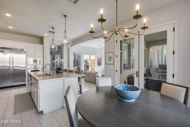 kitchen with sink, decorative light fixtures, white cabinets, built in appliances, and a kitchen island with sink