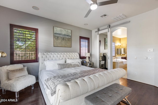 bedroom with connected bathroom, dark wood-type flooring, a barn door, and ceiling fan