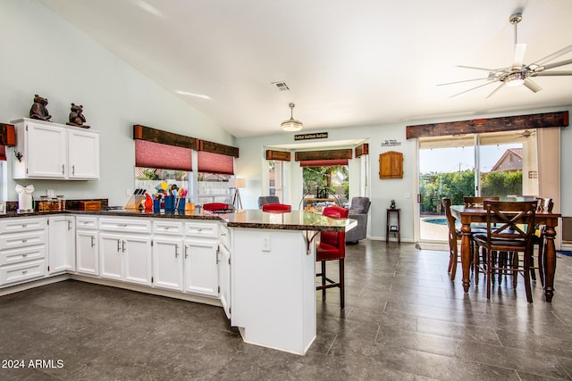 kitchen featuring ceiling fan, white cabinetry, lofted ceiling, and a breakfast bar area