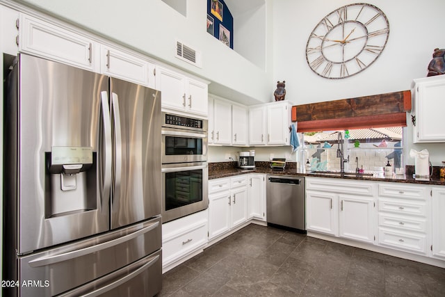 kitchen featuring white cabinets, stainless steel appliances, dark stone counters, and sink