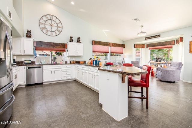 kitchen with a kitchen bar, kitchen peninsula, stainless steel appliances, white cabinets, and lofted ceiling