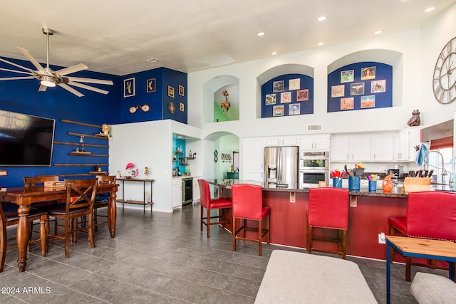 interior space with appliances with stainless steel finishes, a towering ceiling, a breakfast bar, ceiling fan, and white cabinetry