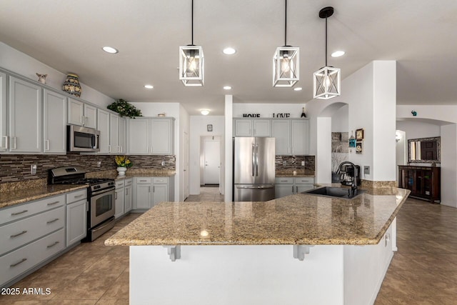 kitchen featuring a breakfast bar, appliances with stainless steel finishes, stone countertops, a sink, and a peninsula