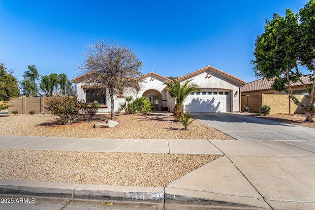 mediterranean / spanish-style house featuring a garage, concrete driveway, a tiled roof, fence, and stucco siding