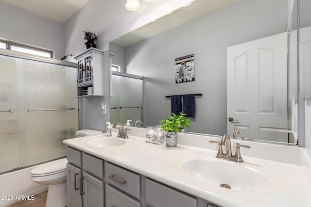 bathroom with toilet, double vanity, bath / shower combo with glass door, and a sink