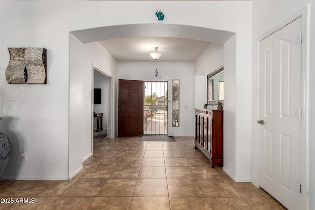 foyer with arched walkways, light tile patterned flooring, and baseboards