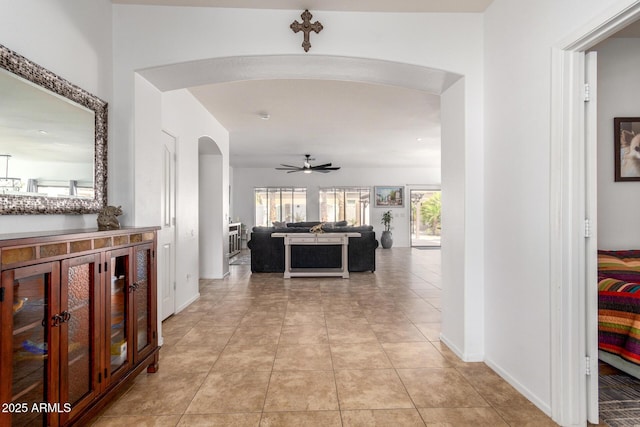 hallway featuring arched walkways, light tile patterned floors, and baseboards