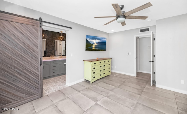 interior space featuring visible vents, ensuite bathroom, a barn door, light tile patterned floors, and baseboards