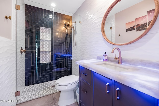 bathroom featuring tile patterned flooring, toilet, vanity, a stall shower, and tile walls