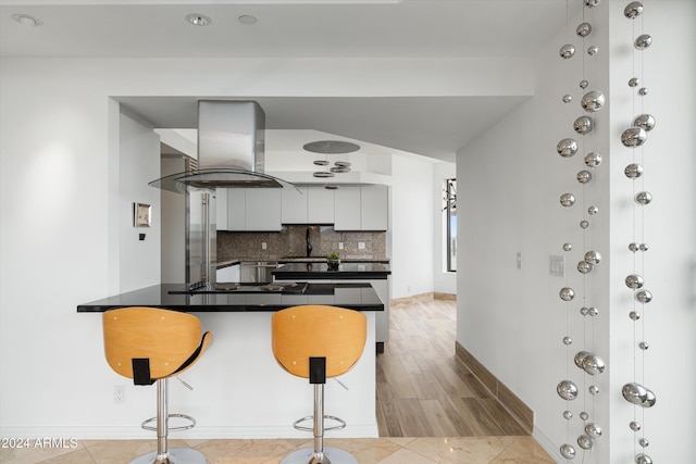 kitchen with backsplash, kitchen peninsula, wall chimney exhaust hood, light hardwood / wood-style floors, and white cabinetry