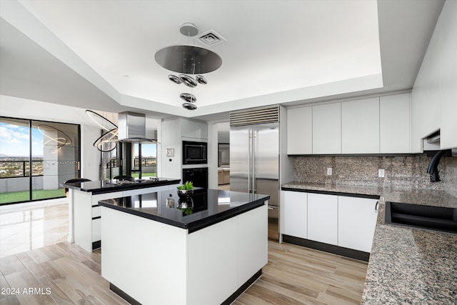 kitchen with white cabinets, a center island, built in appliances, and light hardwood / wood-style flooring