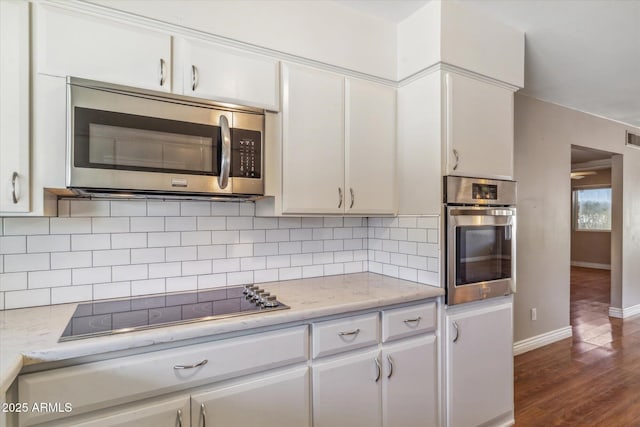 kitchen with backsplash, appliances with stainless steel finishes, dark hardwood / wood-style flooring, light stone countertops, and white cabinets