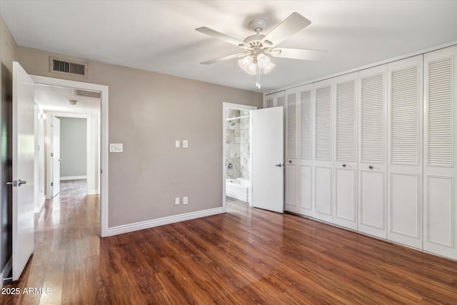 unfurnished bedroom featuring connected bathroom, dark wood-type flooring, a closet, and ceiling fan