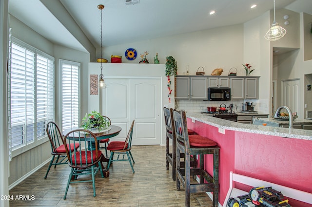 kitchen featuring decorative backsplash, hanging light fixtures, hardwood / wood-style flooring, vaulted ceiling, and gray cabinets