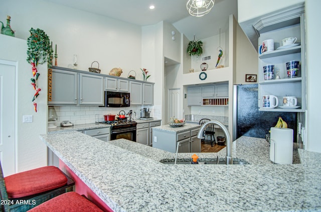 kitchen with a breakfast bar, black appliances, sink, and gray cabinetry