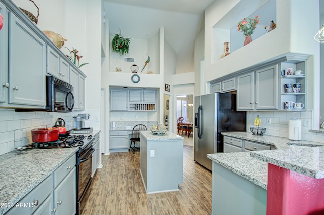 kitchen with appliances with stainless steel finishes, a center island, light stone counters, high vaulted ceiling, and light hardwood / wood-style flooring