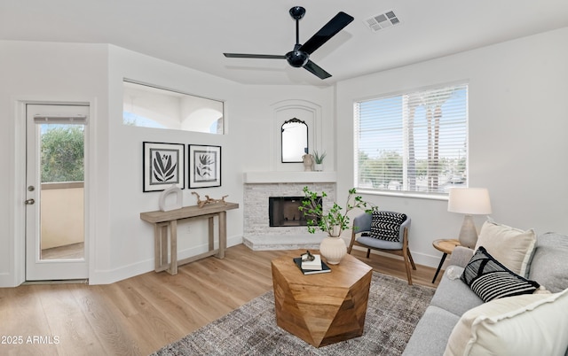 living area featuring a fireplace with raised hearth, wood finished floors, a ceiling fan, visible vents, and baseboards