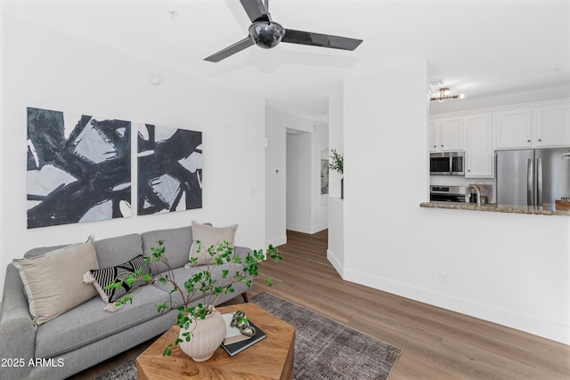 living room with light wood-type flooring, ceiling fan, and baseboards