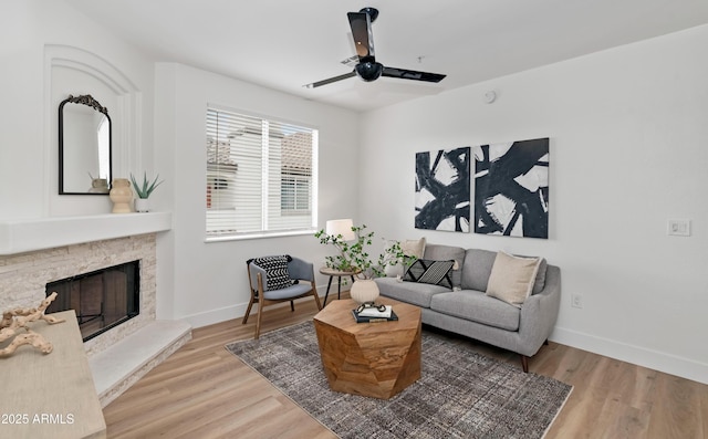 living room featuring a stone fireplace, ceiling fan, light wood-style flooring, and baseboards