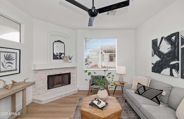 living room featuring baseboards, a stone fireplace, and light wood-style floors