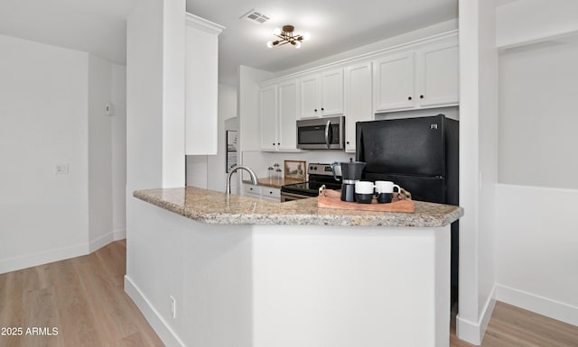 kitchen with white cabinets, light stone counters, kitchen peninsula, stainless steel appliances, and light hardwood / wood-style flooring