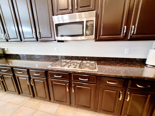 kitchen featuring dark stone counters, light tile patterned floors, dark brown cabinets, and stainless steel appliances