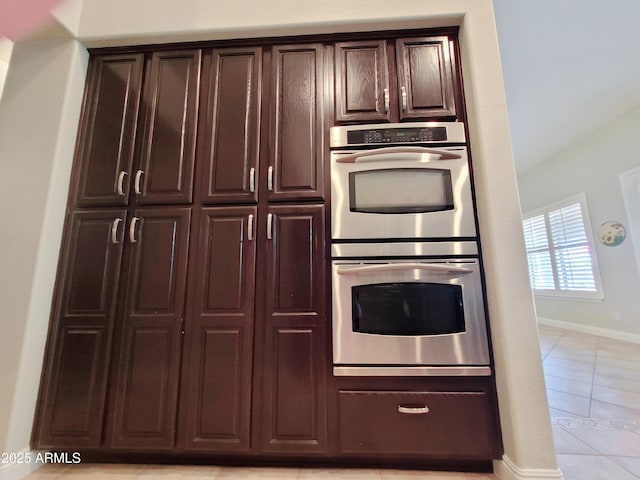 kitchen with light tile patterned floors, baseboards, stainless steel double oven, and dark brown cabinets