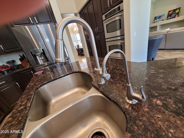 interior details featuring a sink, dark stone counters, appliances with stainless steel finishes, and dark brown cabinetry