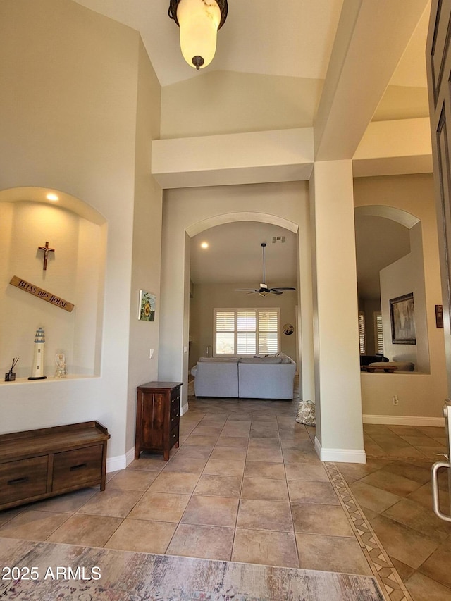 foyer with arched walkways, tile patterned floors, high vaulted ceiling, a ceiling fan, and baseboards
