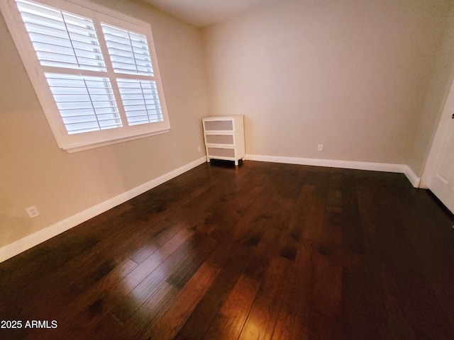 spare room with baseboards and dark wood-type flooring