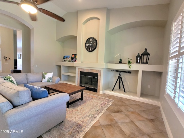 living area featuring ceiling fan, built in features, baseboards, and a fireplace