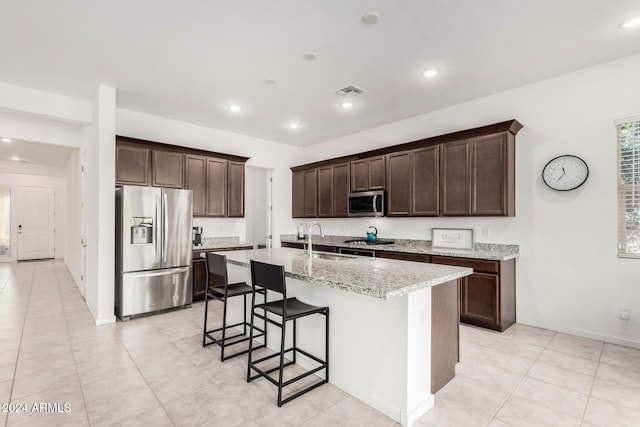 kitchen featuring a breakfast bar, a center island with sink, sink, appliances with stainless steel finishes, and light stone counters