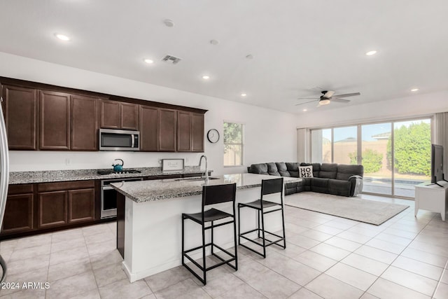 kitchen featuring light stone countertops, sink, ceiling fan, stainless steel appliances, and a kitchen island with sink