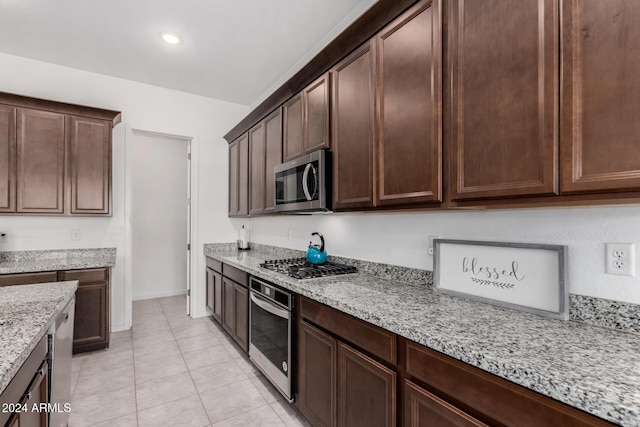 kitchen with dark brown cabinets, light stone counters, light tile patterned floors, and stainless steel appliances