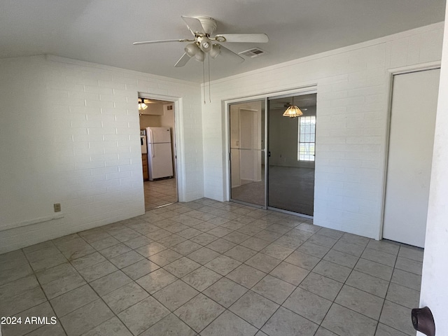 spare room featuring light tile patterned floors, ceiling fan, and brick wall