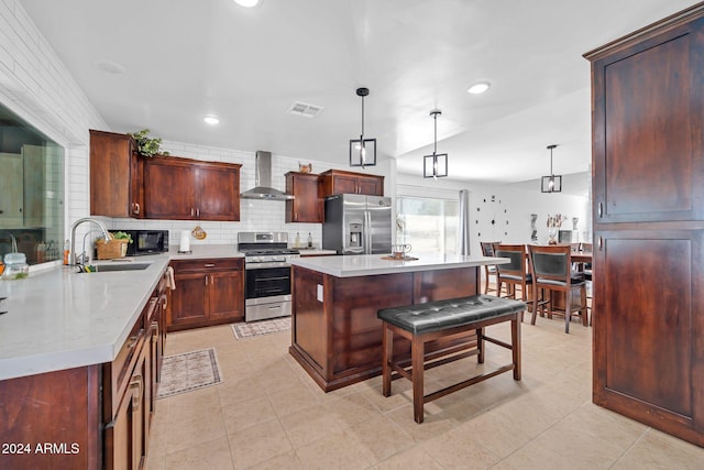 kitchen featuring wall chimney exhaust hood, sink, a center island, decorative light fixtures, and appliances with stainless steel finishes