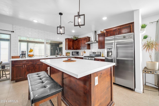 kitchen featuring a kitchen island, wall chimney exhaust hood, stainless steel appliances, a kitchen bar, and decorative light fixtures