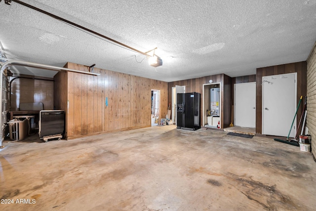 garage with a garage door opener, gas water heater, wooden walls, and black fridge