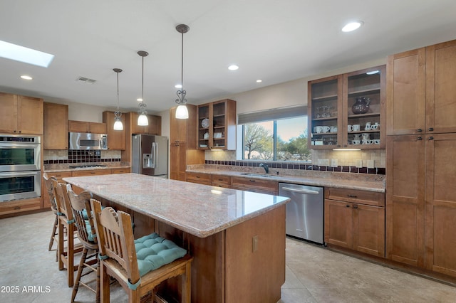 kitchen featuring sink, a breakfast bar, stainless steel appliances, light stone counters, and a kitchen island