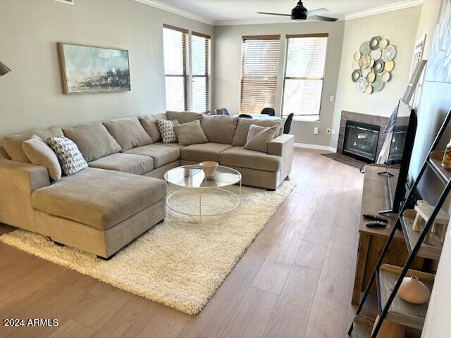 living area with baseboards, ornamental molding, a tile fireplace, wood finished floors, and a ceiling fan