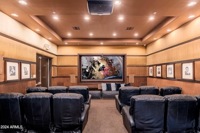 carpeted cinema featuring a tray ceiling, a towering ceiling, visible vents, and wood walls