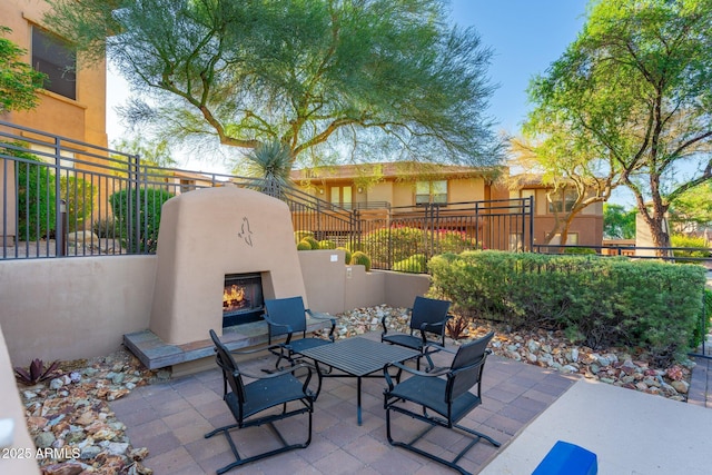 view of patio with fence and a lit fireplace