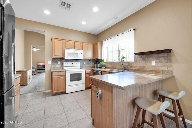 kitchen with sink, a kitchen breakfast bar, kitchen peninsula, light brown cabinetry, and appliances with stainless steel finishes