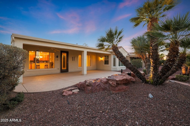 back house at dusk featuring ceiling fan and a patio area