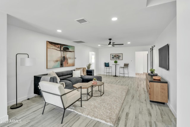 living room with ceiling fan, a barn door, and light hardwood / wood-style floors