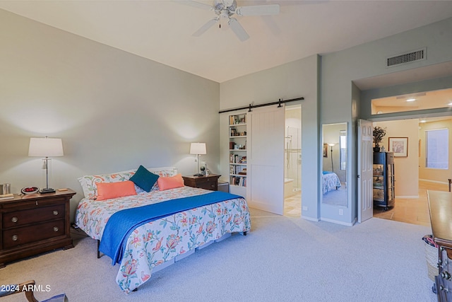 bedroom with ceiling fan, a barn door, light carpet, and ensuite bath