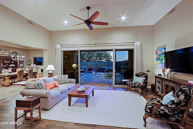 living room with hardwood / wood-style flooring, a towering ceiling, and ceiling fan with notable chandelier